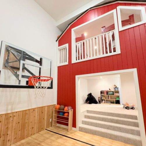 The kid's room in the basement is an absolute delight, featuring a small basketball court, a play area with a barn facade, and a sleeping space with two twin beds.