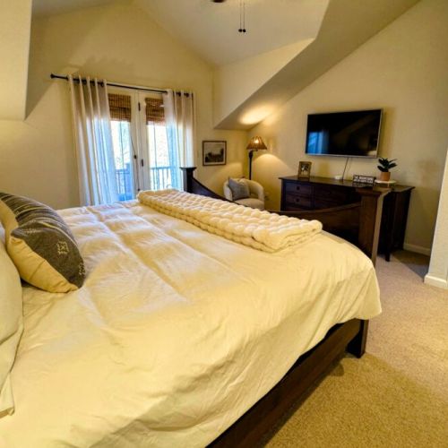 The primary bedroom features a king bed and a large en suite bathroom, as well as a TV and a private balcony facing the woods.