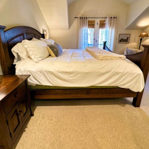 The primary bedroom features a king bed and a large en suite bathroom, as well as a TV and a private balcony facing the woods.